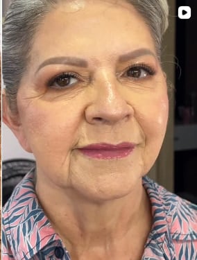 Mujer de cabello canoso con maquillaje de piel luminosa, cejas definidas, sombra neutra y labios en tono vino, con una camisa estampada